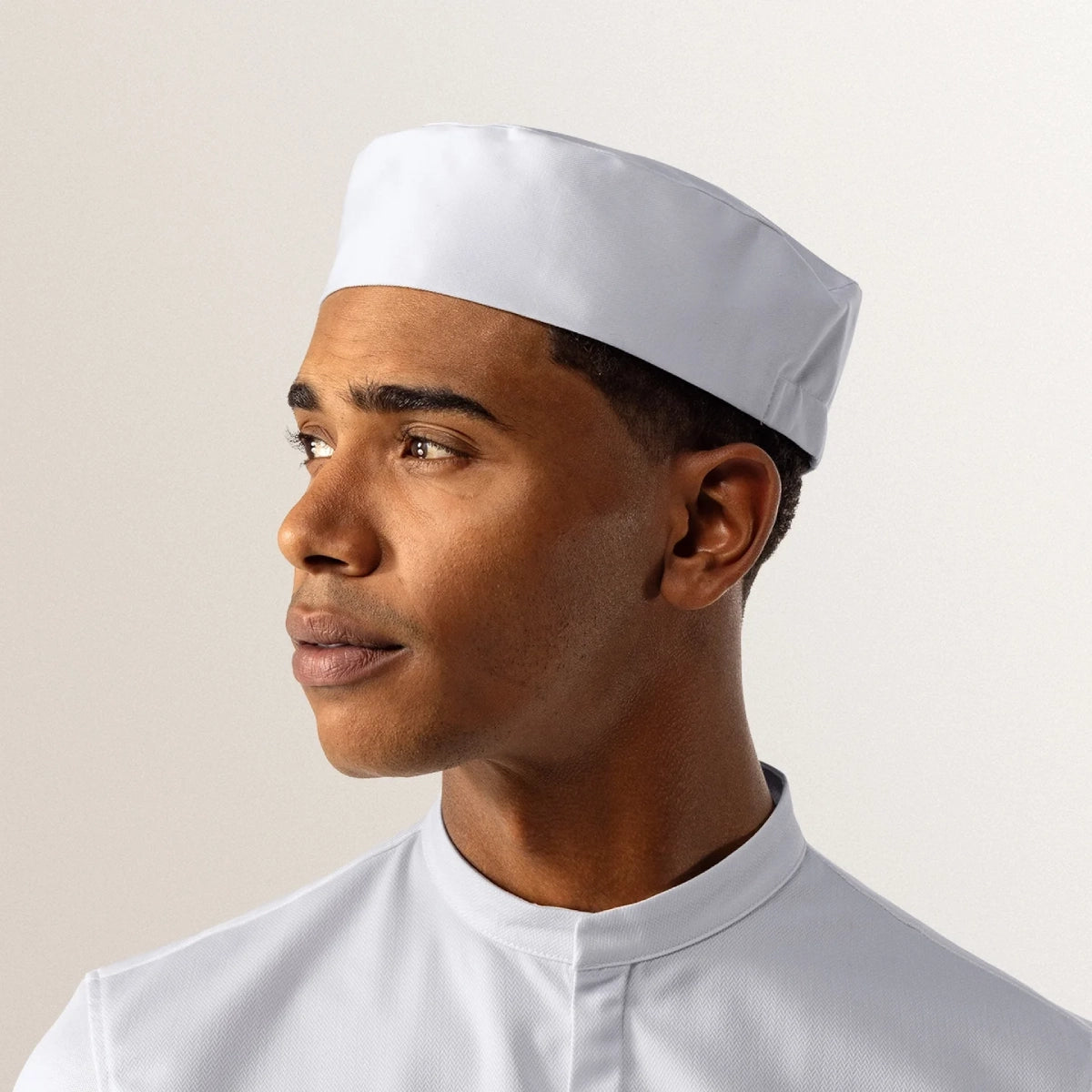 Man wearing a white sailor hat and uniform against a plain background