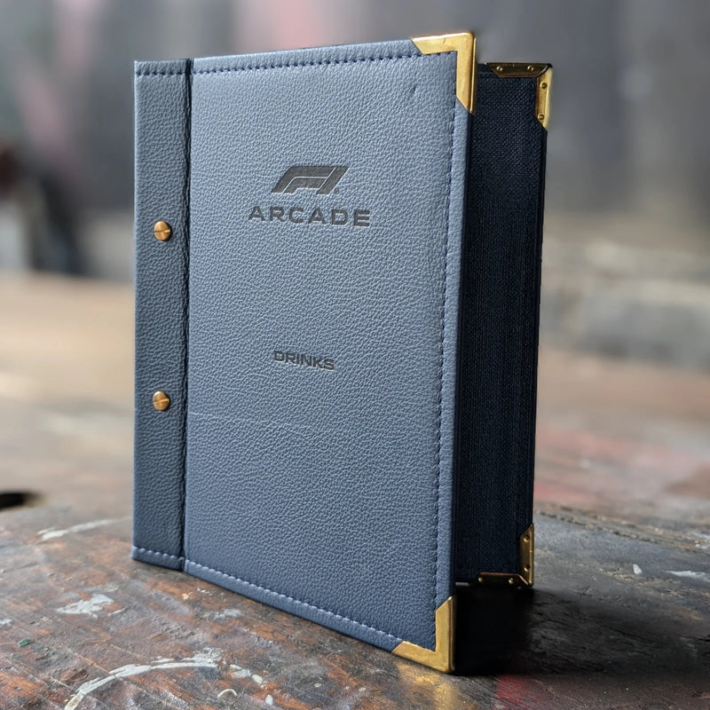 Blue leather menu cover with gold accents on a wooden surface, featuring the Arcade brand.